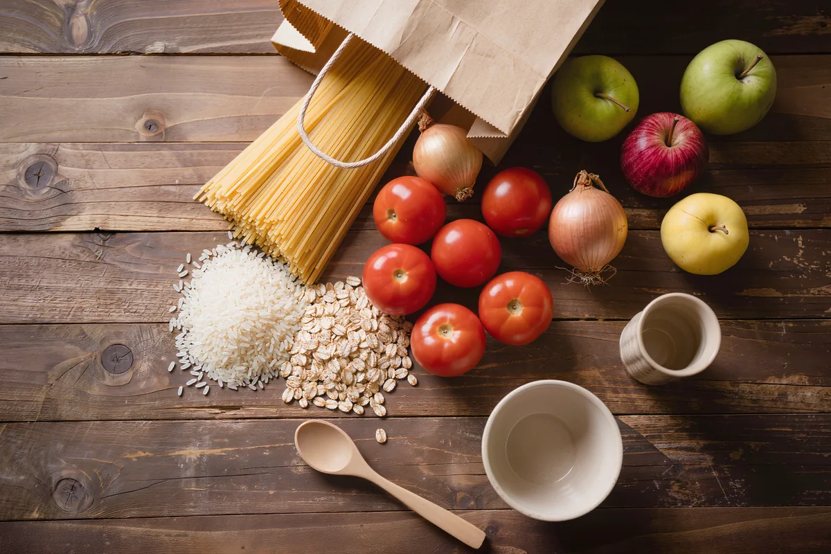 Günstige Basisprodukte für Aldi-Rezepte: Nudeln, Reis, Haferflocken und Tomaten auf einem Tisch